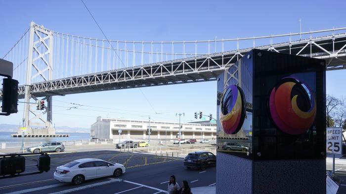 The San Francisco-Oakland Bay Bridge is shown above pedestrians walking next to a Firefox sign at a Mozilla office near the building where a technology executive was fatally stabbed outside of in San Francisco, Wednesday, April 12, 2023. (AP Photo/Jeff Chiu)